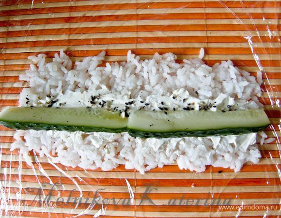 На рис выложите сыр «Филадельфия» небольшой полосой, посыпьте кунжутом. Сверху выложите дольки огурца.