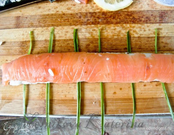 Теперь ролл готов. Его нужно достаточно аккуратно переложить на разделочную доску и нарезать на порционные кусочки. Но если вы увлеклись процессом и хотите придать более эстетичный вид роллу, можно украсить его луковыми перышками. Для этого луковые перышки помойте, просушите, разделите каждое перышко на 3 части. Выложите полоски (длина которых примерно 10 см) на разделочную доску на расстоянии нескольких сантиметров друг от друга. Положите на них ролл и нарежьте так, чтобы полоски лука были посередине каждого кусочка.