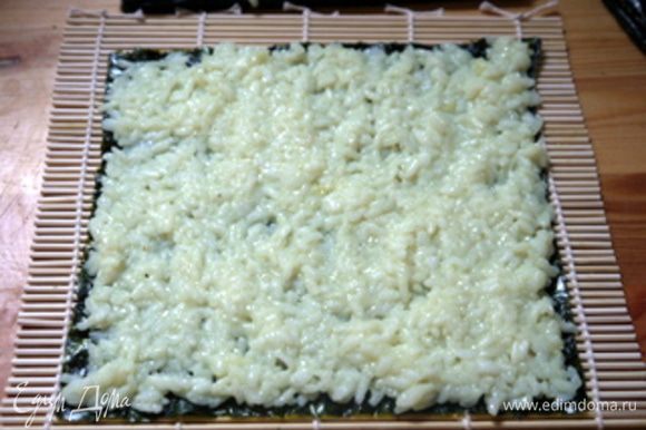 Взять длинный лист нори и распределить по нему приготовленный рис для суши.