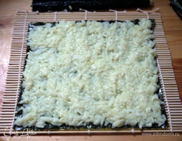 Взять длинный лист нори и распределить по нему приготовленный рис для суши. 