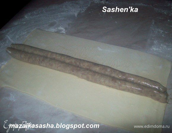 Припылить стол мукой и слегка раскатать слоеное тесто. Выкладываем на него наши сосиски - колбаски.