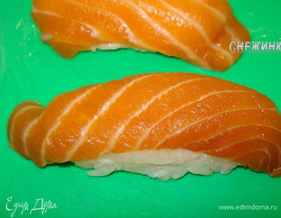 Для того, чтобы рис не прилипал к рукам, необходимо, чтобы рядом с Вами находилась мисочка с водой, смешанной с небольшим количеством рисового уксуса, в которой Вы периодически будете смачивать руки. После того, как опустили ладошки в уксусную воду, сделайте хлопок, чтобы ушла лишняя жидкость. При работе с рисом руки всегда должны быть влажными! Сформируем шарик из риса, весом 15 г. (около 1,5 ст.л.). Теперь возьмите заготовку лосося и положите его на левую руку (для правшей) на нижние фаланги пальцев. Положите посередине шарик риса и, надавливая на него пальцами правой руки сверху, сжимайте ладонь, как будто формируете колбаску. Затем переверните суши рыбой вверх и сожмите еще раз, прижимая рыбу плотнее к рису. 