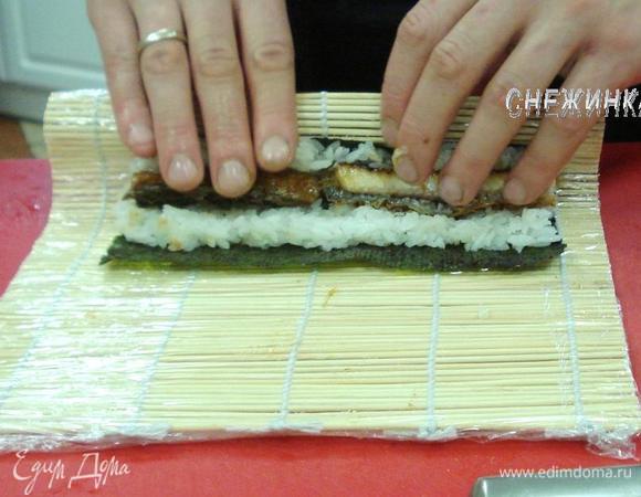 Начинаем сворачивать ролл. Размещаем большие пальцы под коврик и максимально загибаем его, придерживая начинку. Поджимаем ковриком.