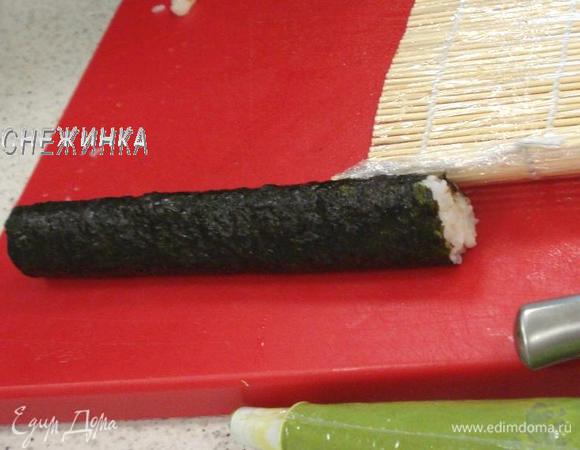 Затем приподнимает коврик и толкаем его вместе с рулетом вперед. Смачиваем остаток нори уксусной водой и окончательно заворачиваем ролл. Прижимаем его немного ковриком, придавая форму. Кстати, ковриком можно придавать и треугольную, и квадратную форму роллов.
