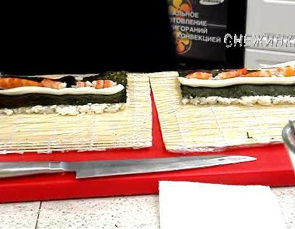 На коврик кладем 0,5 листа нори, распределяем по нему 75 г. риса, здесь занимаем уже всю поверхность. Затем переворачиваем заготовку рисом вниз на коврик. По центру нори высаживаем полоску сливочного сыра. 