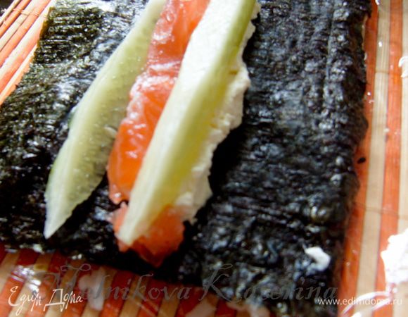 На обратную чистую сторону нори выложить полосу сыра "Филадельфия", на нее выложить полосу лосося, огурца, авокадо. 