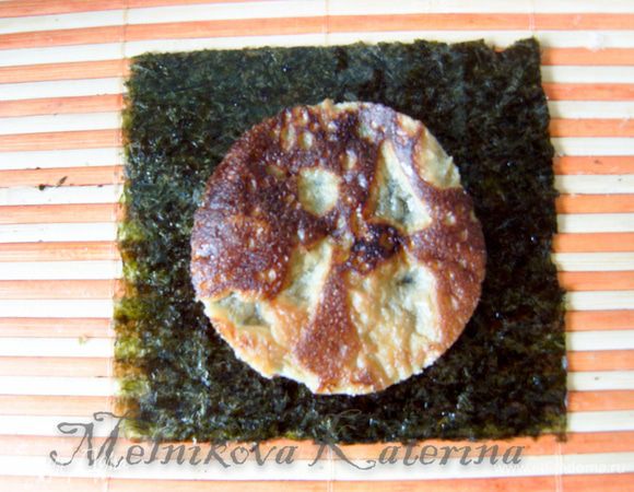 Лист нори разрезать на 4 равные части, на 4 квадрата. Работаем с 1 квадратом. Положить его на коврик для суши, смочить пальцы рисовым уксусом и смазать всю поверхность нори (это необходимо для того, чтобы смягчить лист и было удобно с ним работать). Выложить на нори кружок омлета. 