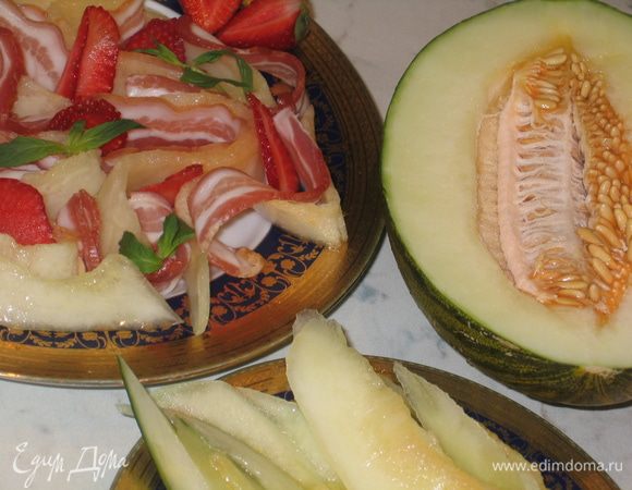 Свиной окорок нарезать тонкими пластинками и выложить на блюдо вместе с дыней, стараясь придать всем ломтикам объем...уложить сверху нарезанную клубнику и украсить веточками мяты
