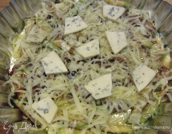 Возьмите круглую форму. Смажьте ее маслом, выложите рис в форму. Попробуйте рис - он должен быть нормально посолен. Если недостаточно - досолите.
Выложите сверху кабачок с луком ровным слоем. Порежьте Дорблю и выложите кусочки сверху. Посыпьте натертым на крупной терке моцареллой. 