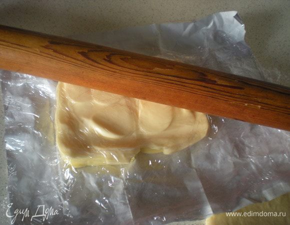 Достаем масло из холодильника,раскрываем упаковку,с бумаги не снимаем,а только сверху накрываем пленкой.Стараемся руками масло не трогать совсем!Скалкой начинаем масло превращать в прямоугольный пласт.Сначала постукиваем,потом поглаживаем.