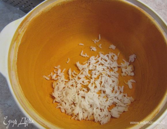 А теперь самое интересное. Смажьте форму изнутри сливочным маслом. У меня керамическая кастрюля около двух литров. Посыпьте изнутри куркумой и поворачиванием кастрюли и постукиванием добейтесь того, чтобы вся куркума равномерно "прилипла" к маслу и обволокла все внутри кастрюли. Выложите порцию риса в кастрюлю ровным слоем. У меня это где-то три крупные горсти.
