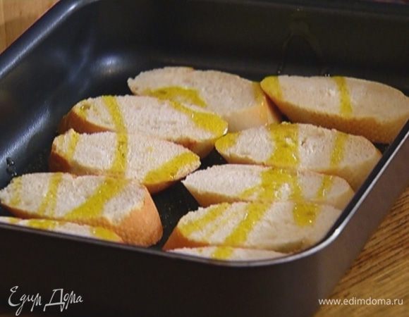 Багет нарезать ломтиками наискосок, выложить на противень, сбрызнуть оливковым маслом и отправить в разогретую духовку на 5–7 минут.