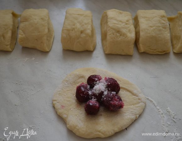 Затем еще раз хорошо вымешиваем, разделяем на 2 части, раскатываем в колбаску, делим на части, раскатать не тонко в лепешку, положить прямо замороженные вишни, присыпать сахаром, защипнуть края, и укладываем на сковородку с толстым дном, швом вниз, не сильно плотно, смазать желтком, выпекать при 190 гр 30 мин.