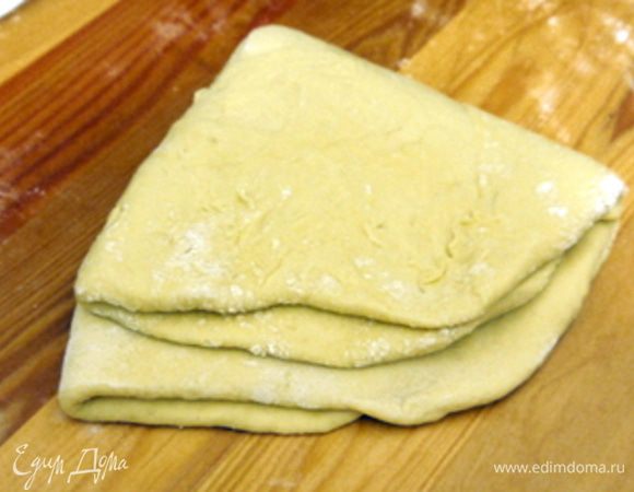 Присыпать рабочую поверхность мукой, перенести на неё тесто, осадить и раскатать его. Сложить раскатанное тесто пополам, затем ещё раз пополам.
