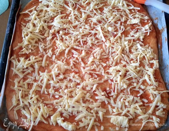 Затем раскатываем тесто, из этого количества продуктов у меня получили две большие пиццы.
Основу для пиццы смазываем томатным соусом и посыпаем тертым сыром.