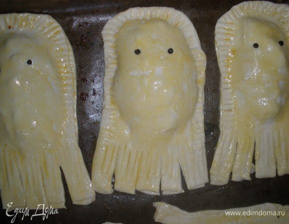 Переложить пирожки на противень, застеленный бумагой для выпечки, смазанный маслом. Сделать надрезы внизу пирожка для ножек-щупалец. Смазать весь пирожок желтком. Воткнуть глазки - это черный перец горошком. 