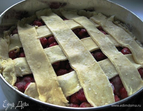 Сверху равномерно разложить кусочки сливочного масла. Раскатать в тонкий пласт вторую часть теста. Ножом разрезать его на полоски примерно 2,5 см и уложить их на пирог крест накрест. Лишнее тесто срезать. Аккуратно завернуть края.