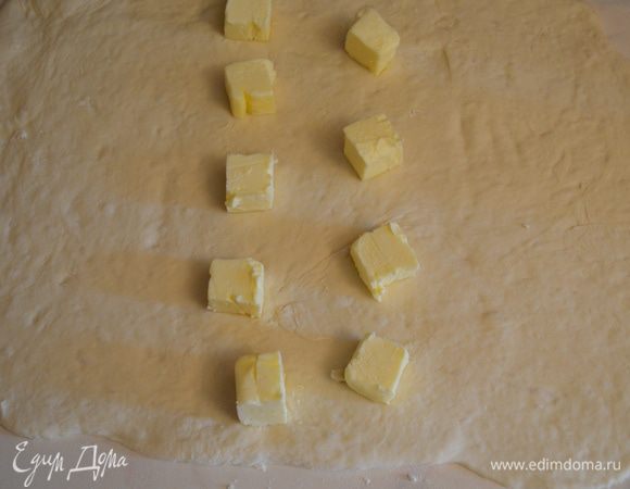 Пласт теста зрительно делим на 3 части. На центральную выкладываем кусочки масла. 