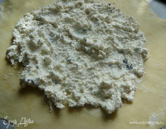 Тесто разделить на две части и раскатать на рабочей поверхности,предварительно присыпав ее мукой. Раскатать тесто в круг. Перенести тесто на противень. Выложить половину творога.
