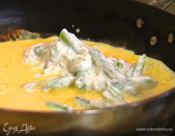 Как только края омлета начнут схватываться, на одну его половину выложить творог со спаржей и листья майорана, накрыть второй половиной омлета и присыпать обжаренными орехами.