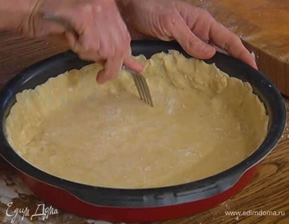 На дно круглой формы выложить круг из бумаги для выпечки и равномерно распределить тесто, сформировав бортики, затем часто наколоть его вилкой.