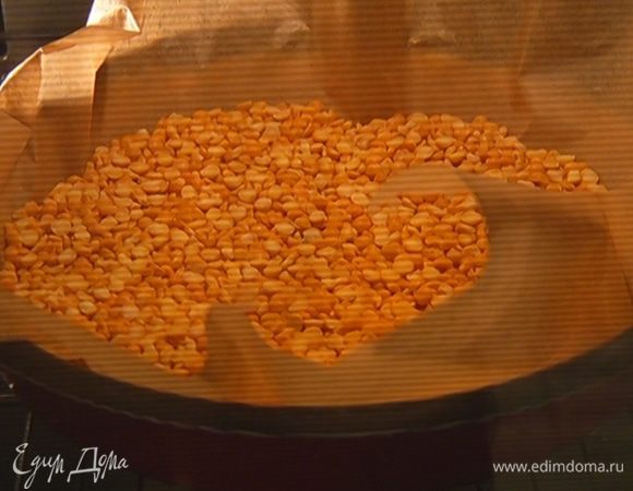 Из бумаги для выпечки вырезать круг, больший по объему, чем форма, выложить на тесто и насыпать сверху 2 стакана гороха или любой крупы.