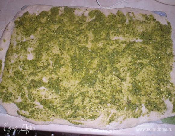 Подошедшее тесто слегка обмять. Раскатать в прямоугольник. Намазать 2-3 ложками соуса песто, равномерно распредилить по всему тесту.