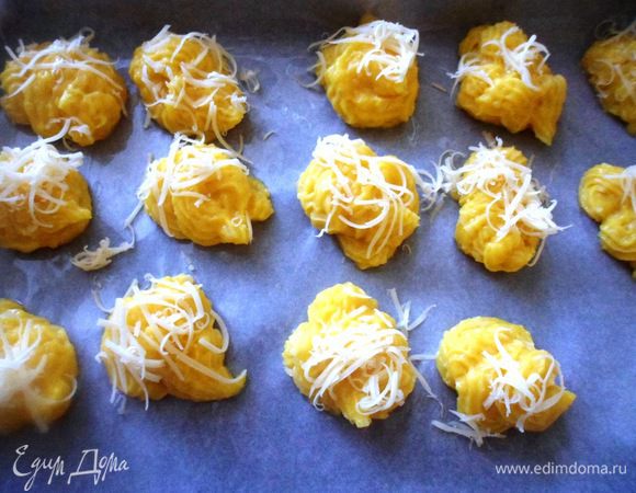 Готовое тесто переложить в кондитерский мешок и отсадить на противень, застеленный бумагой для выпечки, небольшие шарики, посыпать тертым сыром и поставить в разогретую  до 200 градусов духовку на 20 минут