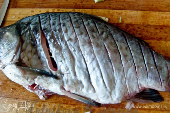Слегка сбрызнуть рыбу лимонным соком. Внутрь положить по два кольца лука. Сделать на рыбе поперечные надрезы ножом глубиной до хребта.