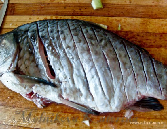 Слегка сбрызнуть рыбу лимонным соком. Внутрь положить по два кольца лука. Сделать на рыбе поперечные надрезы ножом глубиной до хребта. 