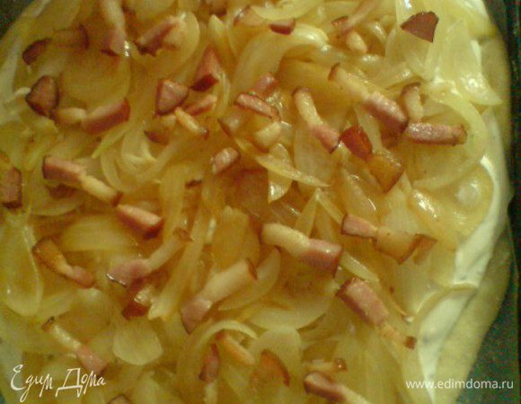 Противень застелить бумагой для выпечки(сверху присыпать мукой). Тесто раскатать и выложить на противень. Сметану смешать с тмином, солью и перцем. Выложить на тесто, равномерно распределить. Сверху разложить лук, грудинку. Выпекать в разогретой до 200 градусов духовку минут 20.