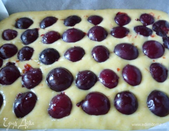 Форму для выпечки выстилаем пергаментом,смазываем маргарином и посыпаем манкой.Выкладываем ровным слоем тесто,затем половинки слив.