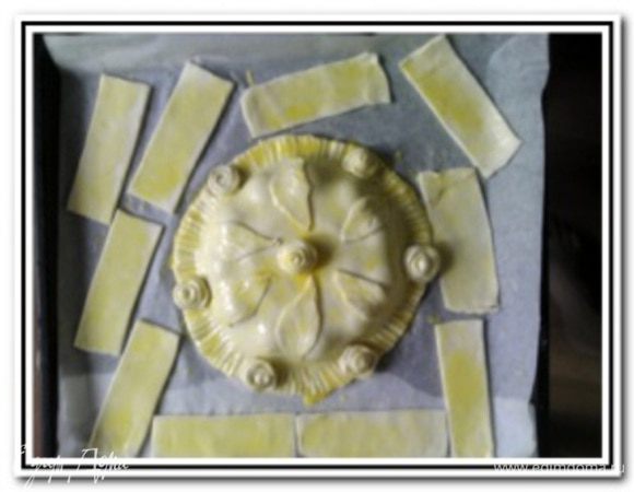 Второй пласт теста также раскатать и вырезать круг. Концы лепешки с сыром смазать водой и накрыть второй лепешкой. Пройти вилкой по основанию и украсить по собственному желанию остатками теста. Желток взбить с небольшим количеством растительного масла и смазать наш пирог.