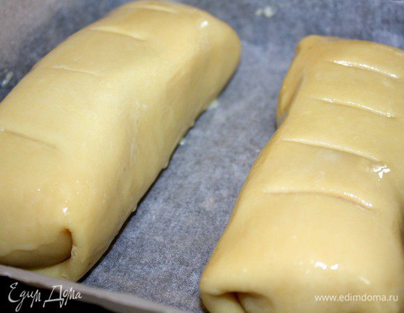 Тесто свернуть конвертом,перевернуть и выложить на противень,застеленный пергаментом,швом вниз.Смазать пирог смесью желтка и молока.Сделать несколько поперечных надрезов и поставить противень в духовку,разогретую до 200*С.