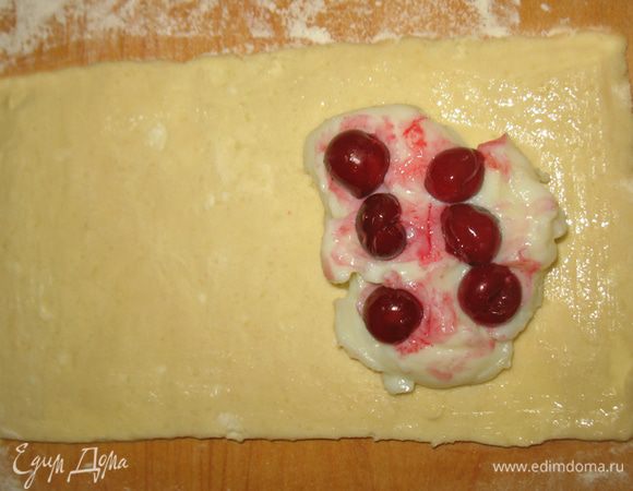 Тесто раскатать тонким слоем и разрезать на прямоугольники 12х20см. Порциями разложить по прямоугольникам пудинг и вишню. Взбить белок и смазать им края прямоугольников. Накрыть тестом начинку и прижать края вилкой.