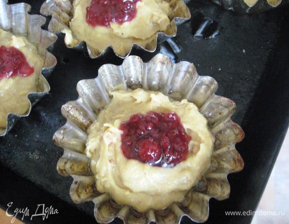 По необходимости смазать маслом и присыпать сухарями высокие формы для маффинов объемом 100-130 мл.
Наполнить формы на 1/3 тестом. Положить в середину теста неполную чайную ложку малинового джема. 