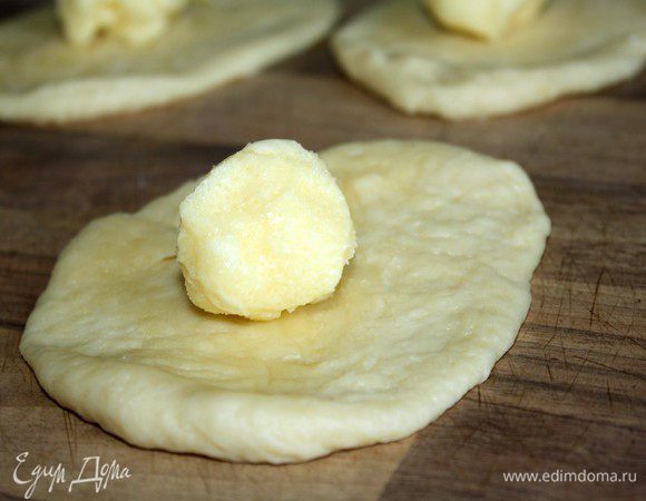 Поднявшееся тесто разделить на небольшие (50 гр) кусочки. Размять каждый из них на присыпанном мукой столе в небольшую лепёшку. Охлаждённую начинку разделить по количеству лепёшек и выложить на каждую масляный шарик.