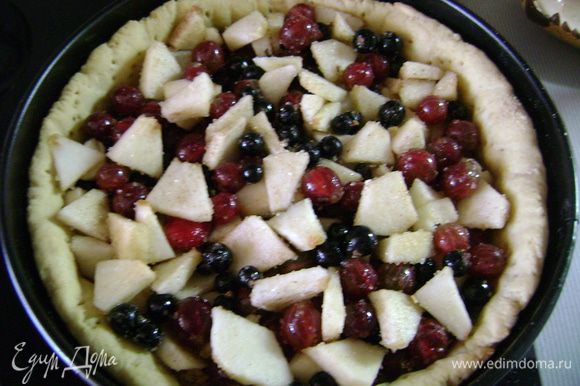 Вытащить корж из духовки, убрать горох или фасоль, вытащить пергаментную бумагу. Посыпать корж толченым печеньем или сухарями и выложить ягоды и яблоки. Отправить в духовку на 10 минут.