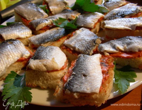 Собираем закусочку. Хлебушек режем на небольшие квадратики/прямоугольнички, смазываем томатным маслом и выкладываем кусочек сельди. И так до конца. Лучше такую закусочку готовить непосредственно перед подачей на стол, так как в холодильник ее ставить нельзя - хлеб отсыреет и не будет хрустящим. Украшаем зеленью по вкусу и подаем. Приятного аппетита)
