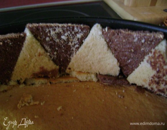 На дно разъемной формы выложить бисквит, который выпекался в этой форме. Край выложить треугольниками, чередуя белый с коричневым. 