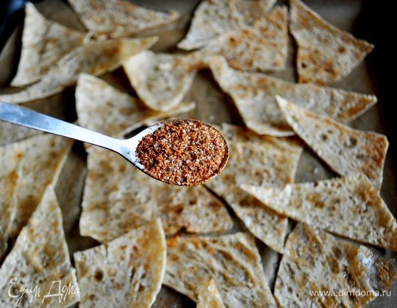 Лаваш нарезать ножницами на треугольные или ромбовидные куски небольшого размера, уложить в один слой на два застелённых бумагой для выпечки противня, полить лаваш маслом, перемешать, чтобы масло распределилось равномерно, посыпать специями, перемешать.
