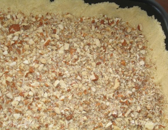 Орехи помолоть в блендере или нарезать ножом...Высыпать крошку в форму и приподнять края, прижимая пальцами тесто к стенкам формы (надо оставить 1/5 часть крошки для обсыпки)...сверху разложить молотые орехи и присыпать немного сахаром (2 ст.л.)