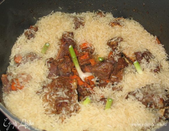 Молодой чеснок промыть и целыми головками выложить среди мяса...всыпать рис по краям казана (если использовать пропаренный рис, то предварительно замачивать его не надо...если обычный рис, то лучше его замочить в холодной воде на 1 час)