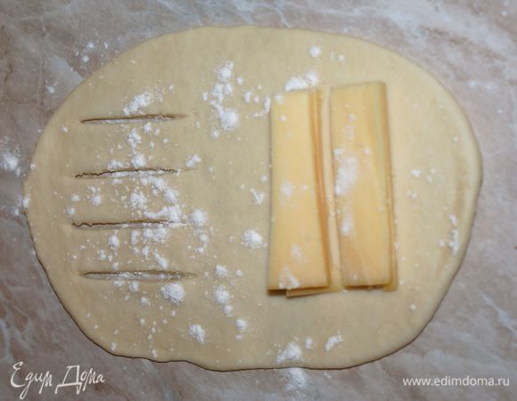 Тесто разделить на 8-10 частей и на смазанном растительным маслом столе раскатать каждую часть в овальную лепешку. На узкий край овала положить порцию нарезанного брусочками сыра. На свободной половине теста сделать три продольных разреза, не доходя до края лепешки.