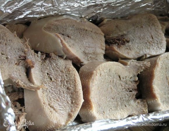 Форму для запекания застелить фольгой. Выложить отварной язык нарезанный ломтиками. Посолить, поперчить.