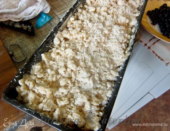 Для штрейзеля к размягченному сливочному маслу добавить муку, сахар, кокосовую стружку и руками сделать крошки. Выложить штрейзель на чернику. 
