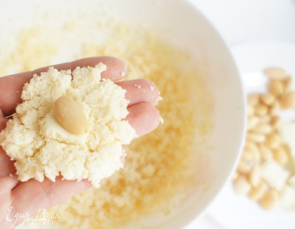 Взять руками небольшое количество теста, сделать лепешечку и положить в центр кусочек белого шоколада и миндаль.