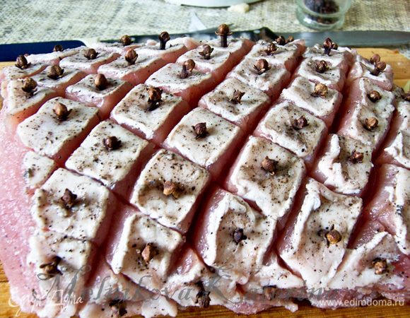 Острым ножом со стороны сальной части сделать диагональные надрезы глубиной 0,5 см сперва в одну сторону, потом в другую, чтобы образовались квадратики-ромбики. Затем острым тонким ножом в каждом квадратике сделать небольшое углубление и вставить бутончик гвоздики. 