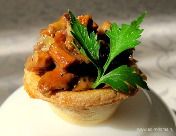 Тарталетки с грибами. Грибы очистить и некрупно порезать. Выложить на сухую сковороду и дождаться когда лисички дадут сок. Потушить на среднем огне до выпаривания сока. Затем добавить  растительное масло и обжарить грибочки до золотистой корочки. В отдельной сковороде поджарить мелко порезанный лук. Смешать ингредиенты и добавить тертый сыр. Выложить в тарталетки, украсить зеленью петрушки.