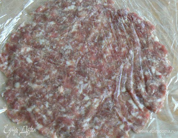 Возьмите 2 листа целлофана, на один из них положите одну порцию мясного фарша, другим листом накройте сверху. Расплющите в тонкую лепешку.